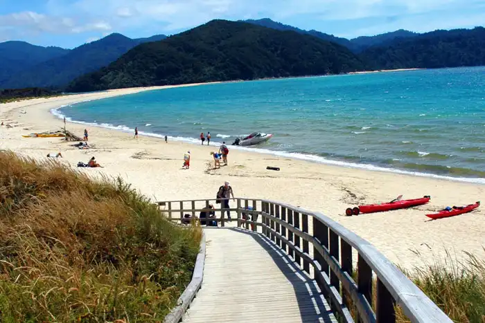 View of Awaroa Beach with sunbavers, kayaks and walkers on the sand