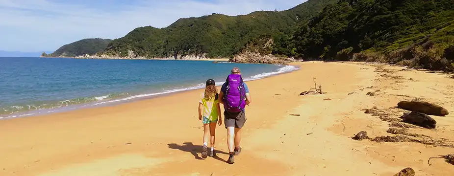 A man and girl walking on an empty gold sand beach in the Abel Tasman