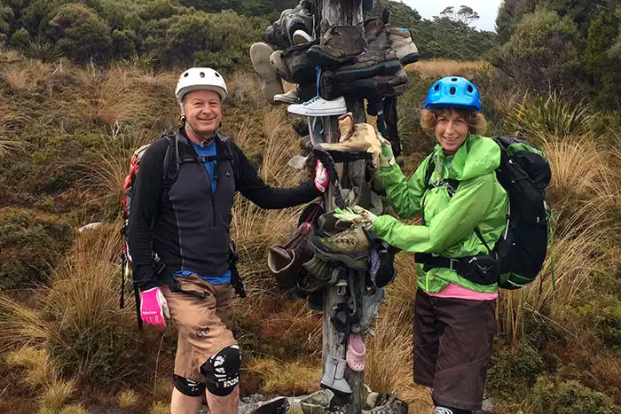 Two bikers pose in front of the boot tree (a post with old boots hung on it) on the Gouland Downs, Heaphy Track