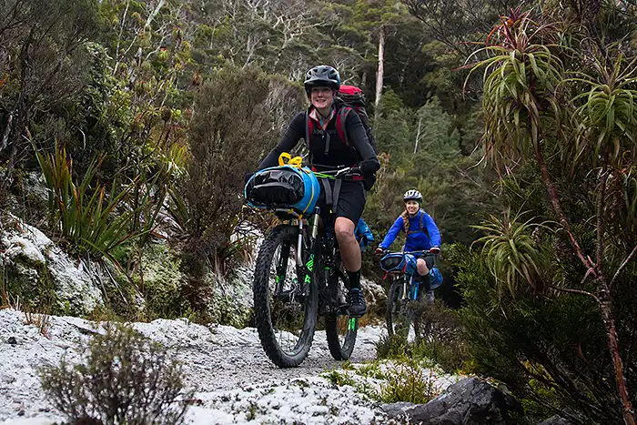 Heaphy Track riders with light snow on the bush-lined track