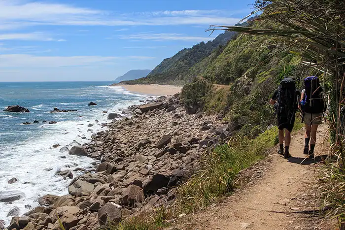 Two trampers walk along the Heaphy coast heading towards Heaphy Hut