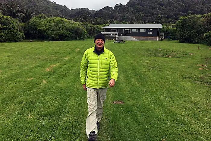 A happy tramper strides down the large green lawn in front of the Heaphy Hut