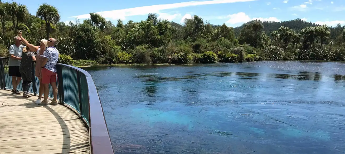 Visitors on viewing paltform at Te Waikoropupu Springs take a selfie with clear blue water bubbling up in their background