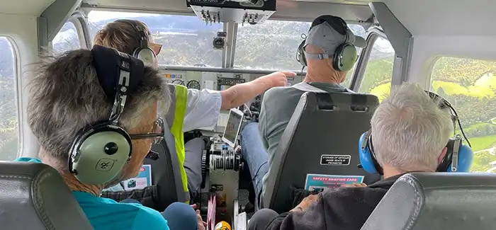 Pilot points our interesting features on the ground to passengers wearing headsets in Golden Bay Air Airvan
