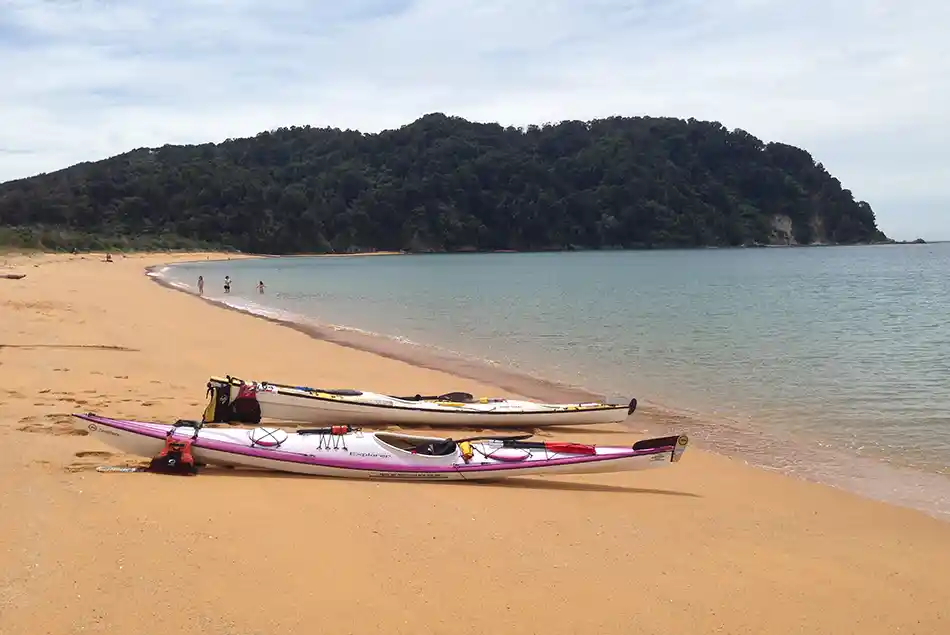 Kayaks laid up on golden sand Totaranui Beach