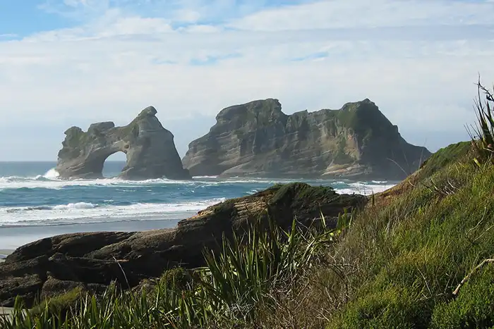 Moody view of the Archway Islands, Wharariki Beach with flax and ridge in foregound